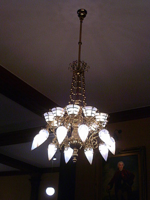 [A chandelier hangs from the ceiling with ten conical bulbs at the end. Above those bulbs are a different type of light. The entire thing is quite ornate, but stately.]